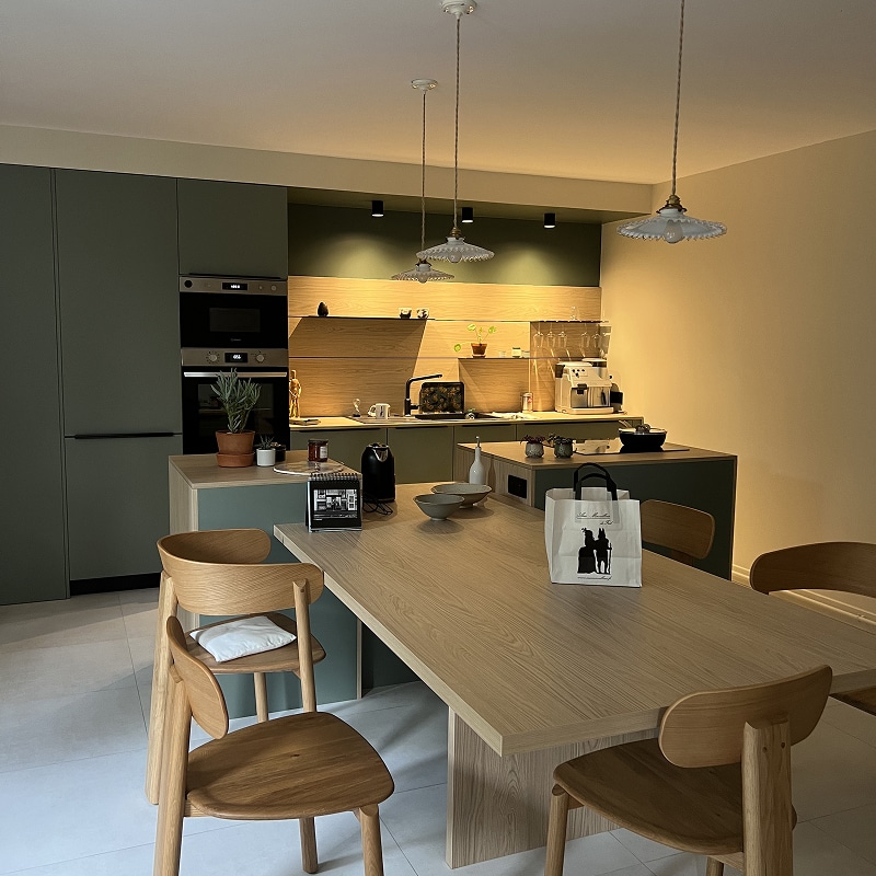 Cuisine Moderne Bois Clair, Vert Sauge et Design Scandinave Cuisine moderne avec armoires vert sauge, îlot central, table à manger en bois clair et chaises en bois courbé, éclairée par des suspensions vintage.