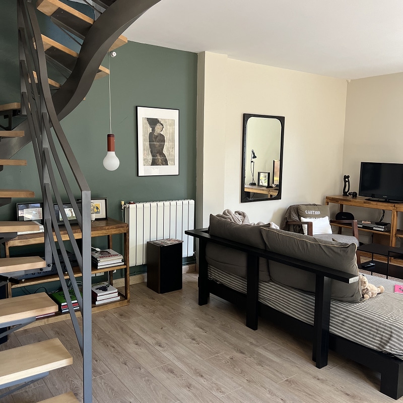 Salon Moderne Design: Escalier, Mur Vert Forêt & Déco Salon moderne avec escalier hélicoïdal métallique, mur vert forêt, suspension design, tableau noir et blanc, et canapé bas noir.